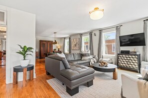 Ein modernes Wohnzimmer mit einem Ecksofa, einem Essbereich mit Billardtisch und einer Küche im Hintergrund.