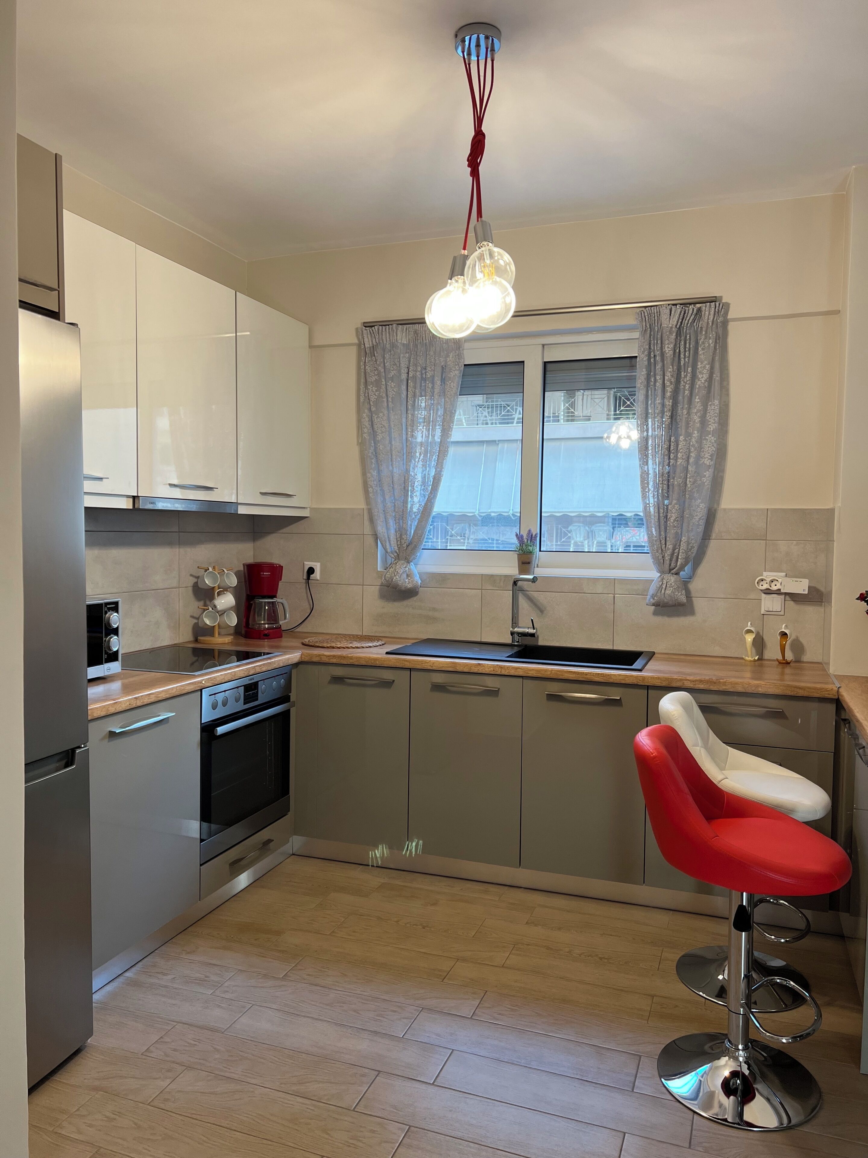 A modern kitchen with stainless steel appliances, a wooden countertop, and a red bar stool.