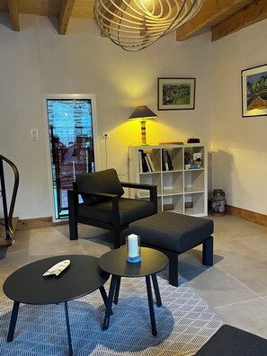 Ett modernt vardagsrum med en soffa, två små bord, en lampa, en bokhylla och en dörr med utsikt.