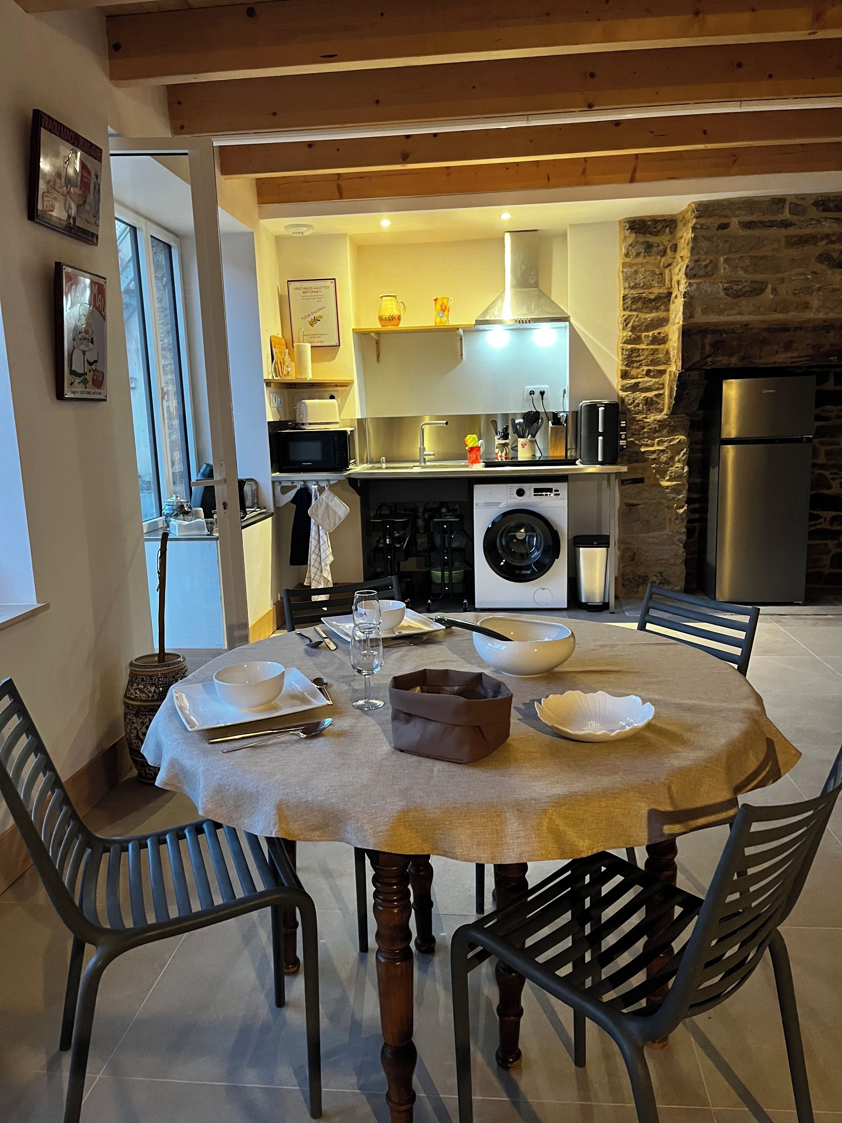A dining area with a round table, chairs, and a kitchen in the background.