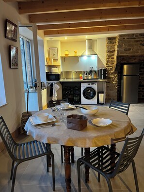 A dining area with a round table, chairs, and a kitchen in the background. - A small house in a private courtyard in the heart of Pont-Aven, across from the museum (Pont-Aven)