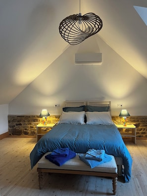 Ein Schlafzimmer mit schrägem Dach, einem Bett mit blauer Bettwäsche, zwei Nachttischlampen und einer Pendelleuchte.