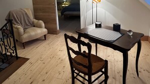 Et hyggeligt soveværelse på loftet med seng, stol, bord og skrivebord. Der er en loftlampe og et vindue med udsigt.