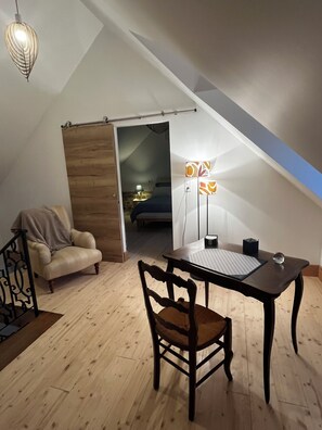 Ein gemütliches Schlafzimmer im Dachgeschoss mit Bett, Stuhl, Tisch und Schreibtisch. Eine Deckenleuchte und ein Fenster mit Ausblick sind vorhanden.