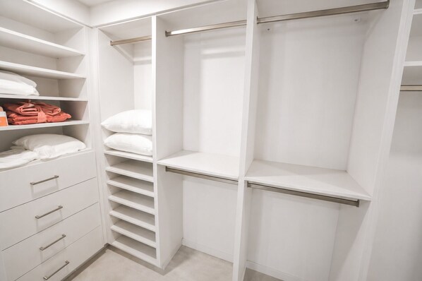 Un placard blanc doté de nombreuses étagères, de tiroirs et d’un espace pour suspendre les vêtements.