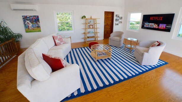 A modern living room with a striped rug, white sofas, a coffee table, and a TV displaying Netflix. - Private Dock - Sunset Ocean Views - Sleeps 9 - 3 Kings - 5 Min Walk to Beach (Southampton)