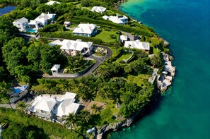 Vue aérienne d’un quartier résidentiel situé sur la côte, avec de nombreuses maisons, une route sinueuse et des eaux d’un bleu limpide.