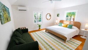 A bedroom with a bed, a green sofa, a patterned rug, and a window with a view of trees. - Private Dock - Sunset Ocean Views - Sleeps 9 - 3 Kings - 5 Min Walk to Beach (Southampton)