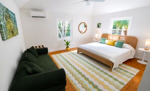 A bedroom with a bed, a green sofa, a patterned rug, and a window with a view of trees. - Private Dock - Sunset Ocean Views - Sleeps 9 - 3 Kings - 5 Min Walk to Beach (Southampton)
