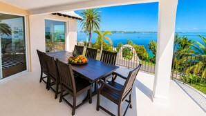 A balcony with a dining table and chairs, a fruit bowl, and a view of the sea and palm trees. - Private Dock - Sunset Ocean Views - Sleeps 9 - 3 Kings - 5 Min Walk to Beach (Southampton)