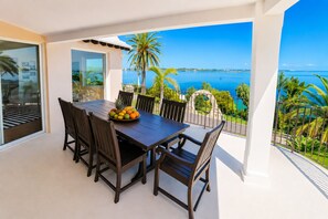 A balcony with a dining table and chairs, a fruit bowl, and a view of the sea and palm trees. - Private Dock - Sunset Ocean Views - Sleeps 9 - 3 Kings - 5 Min Walk to Beach (Southampton)