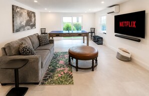 Un salon moderne comprenant un canapé, un pouf, une table basse et un téléviseur fixé au mur.