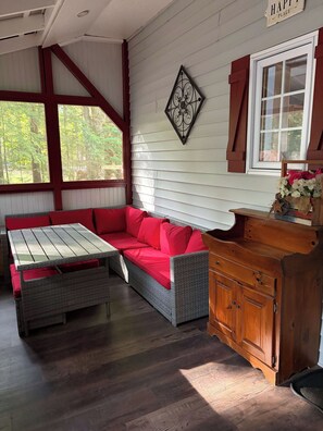 A covered porch with a wicker sofa, a wooden table, and a cabinet.