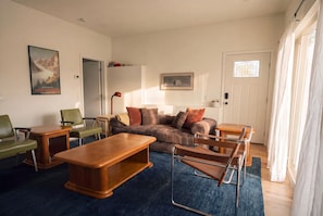 Una sala de estar con un sofá, una mesa de centro de madera, una silla verde, una silla de cuero marrón y una lámpara.