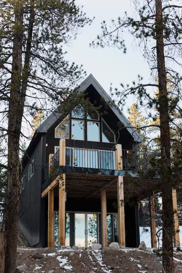 A modern cabin with a balcony, surrounded by trees, and a view of the landscape.
