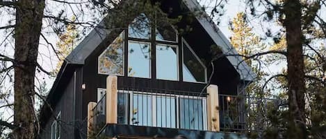 Una cabaña moderna con balcón, rodeada de árboles y vistas al paisaje.