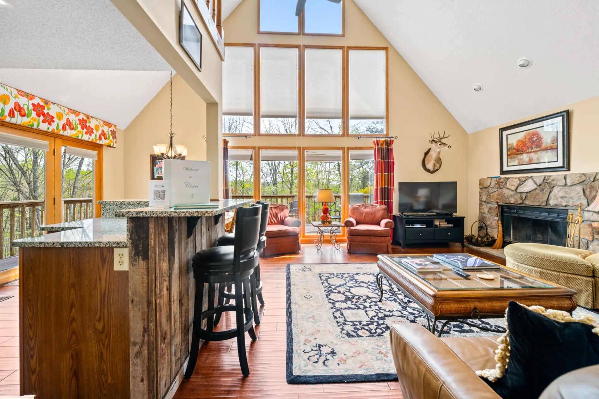 A spacious living area with a high ceiling, a fireplace, a television, and a bar area with stools.