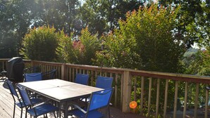 Une terrasse extérieure avec une table et des chaises, entourée d’une balustrade en bois et d’une végétation luxuriante.