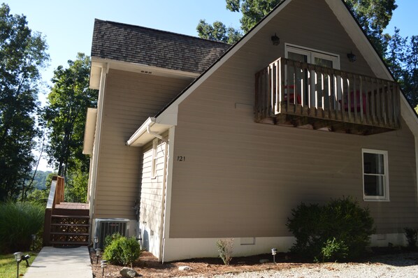 A two-story house with a balcony, a visible number '121' on the side, and a small garden area with shrubs.
