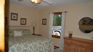 Une chambre à coucher avec un lit, une commode, une lampe et une fenêtre avec des rideaux.