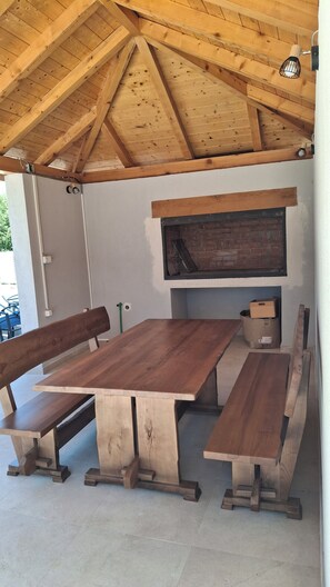 An outdoor wooden dining area with benches and a brick fireplace. - Holiday house Dinko, Sučići 4, Mirlović Zagora (Mirlović Zagora)