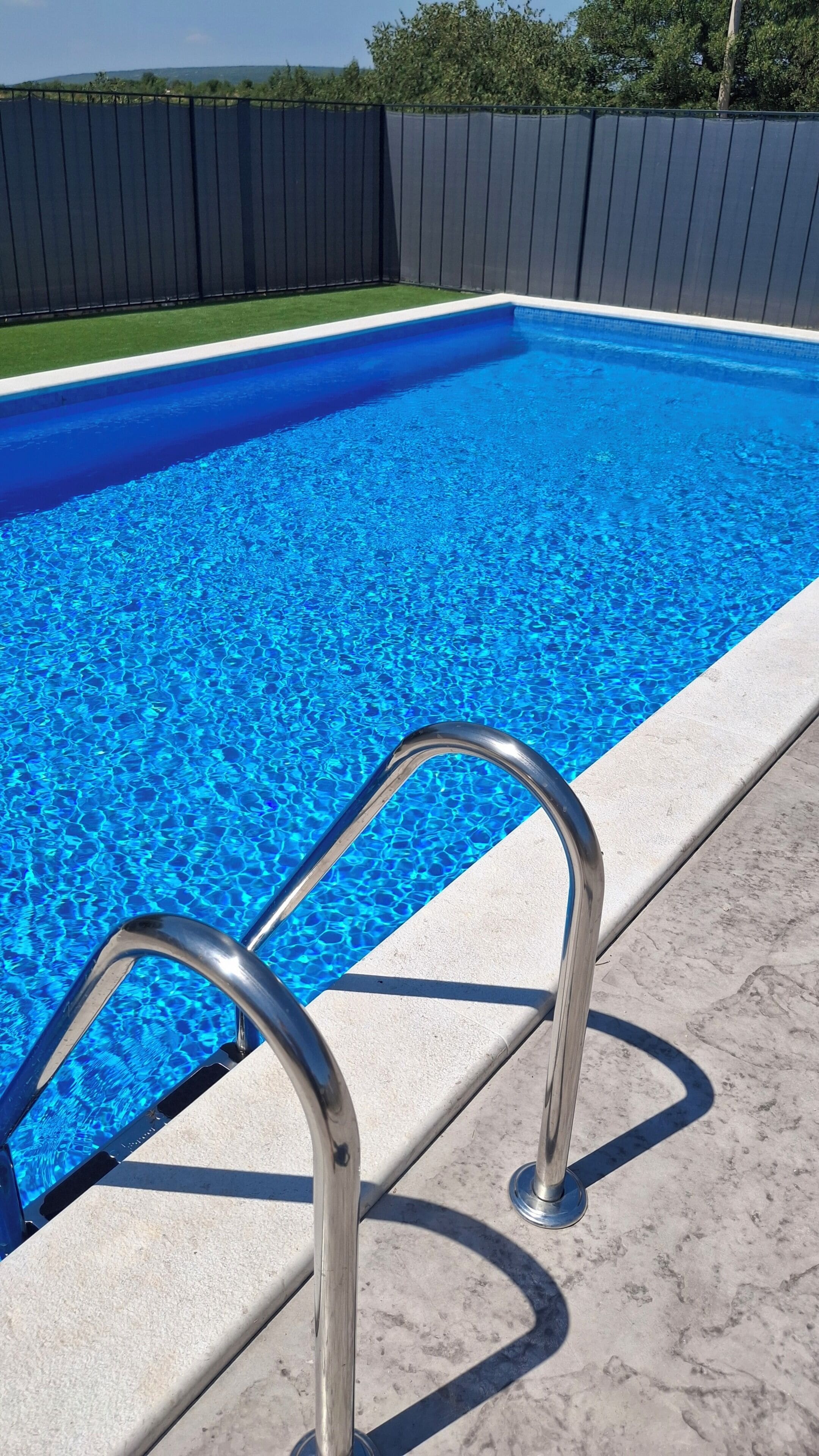 Een zwembad met helderblauw water en een metalen trap.
