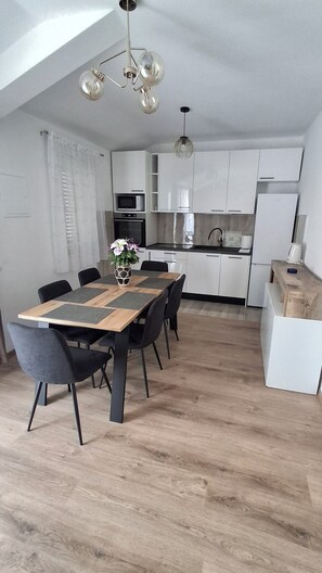 Een moderne keuken met witte kasten, een eettafel met stoelen en een hanglamp.