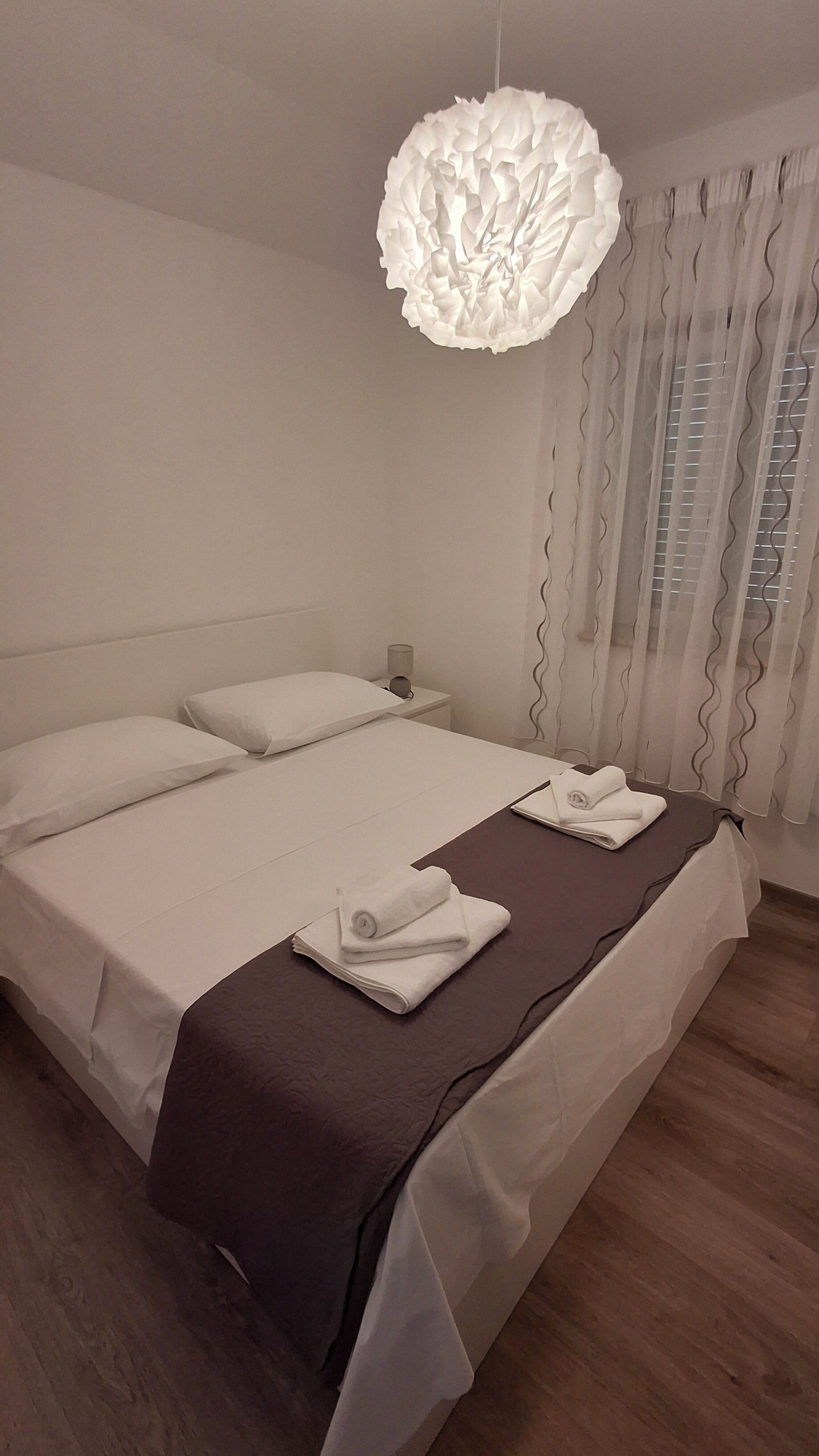 A neatly made bed with a brown bedspread, white pillows, and folded towels on a wooden floor.