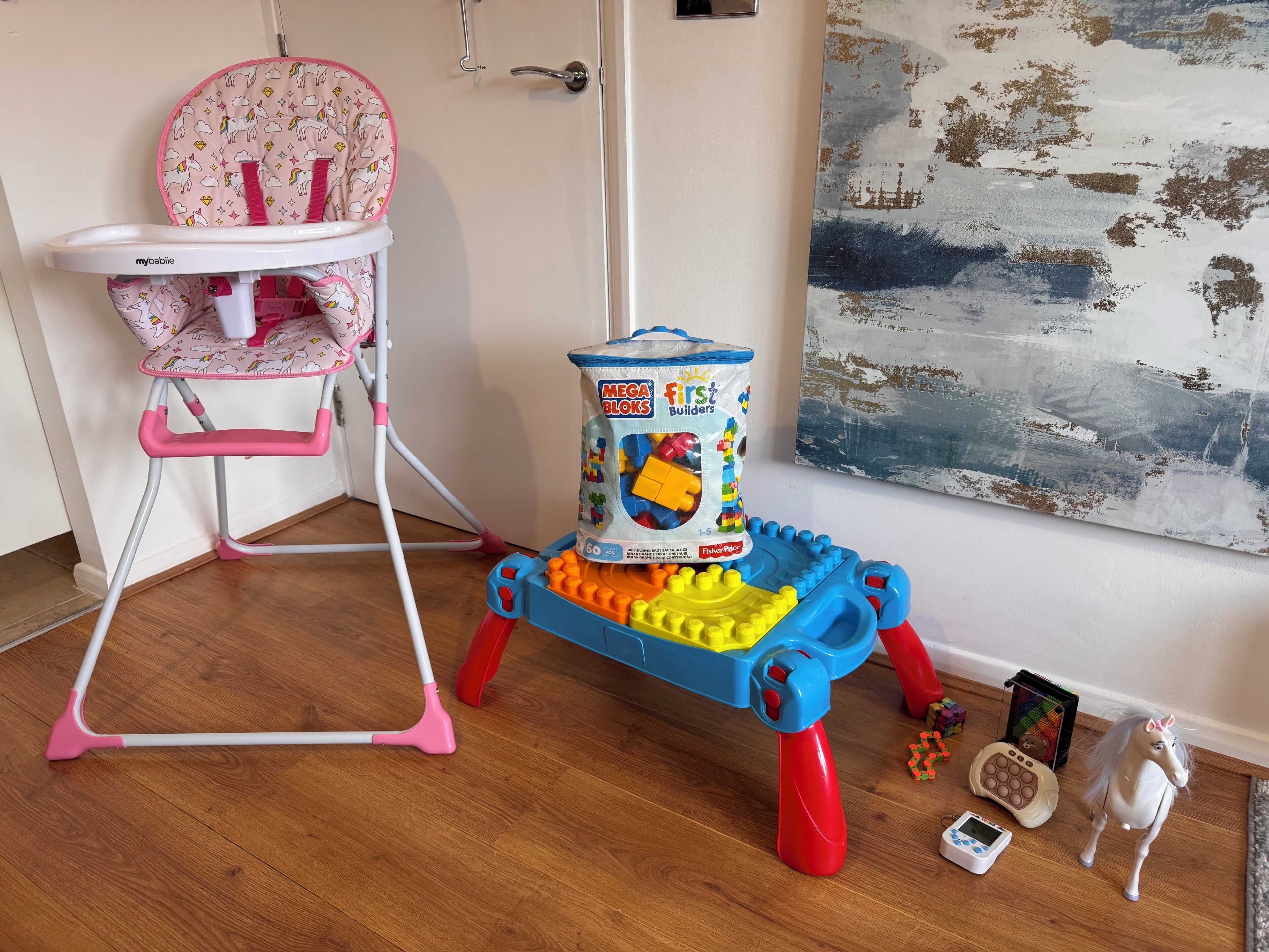 En høj stol til børn, et legetøjsbyggeri og en legetøjshest på et trægulv.