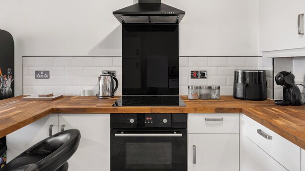 Una cocina moderna con extractor negro, electrodomésticos de acero inoxidable y encimera de madera.