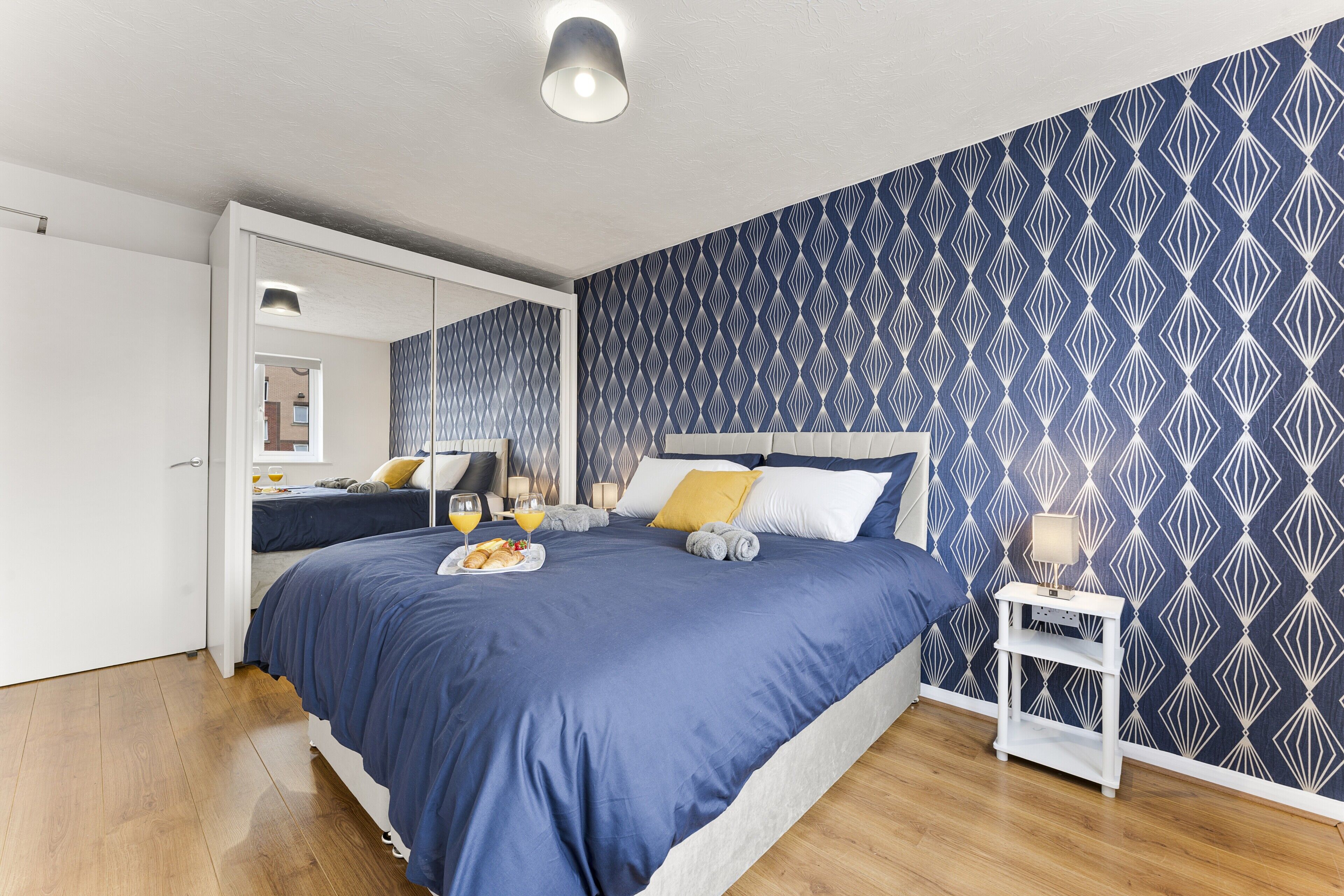 A bedroom with a large bed, bedside tables, a wardrobe, and a patterned wall.