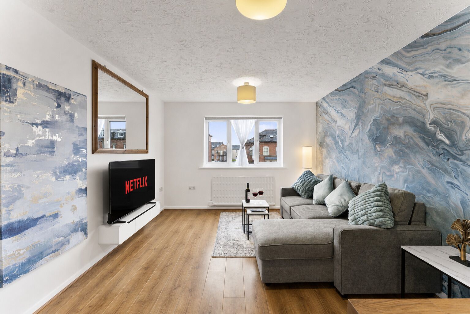 Ein modernes Wohnzimmer mit Flachbildfernseher, grauem Sofa, Couchtisch und Wand mit Marmoroptik.