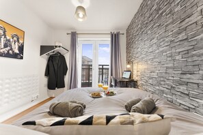 A hotel room with a bed, a laptop on a side table, a breakfast tray, and a view of the outside. - Central Derby 2-Bed | Arcade, Free Parking, King Bed & Ultrafast Wi-Fi (Derby)