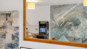 Una habitación con pared de mármol, una consola de videojuegos y un espejo que refleja el ambiente.