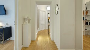 A hallway with a wooden floor, white walls, a white door, and a bookshelf on the right. - Prati Design Home (Roma)