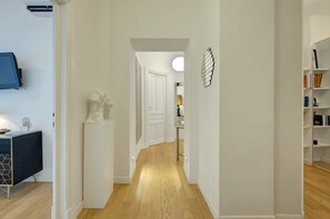 A hallway with a wooden floor, white walls, a white door, and a bookshelf on the right. - Prati Design Home (Roma)
