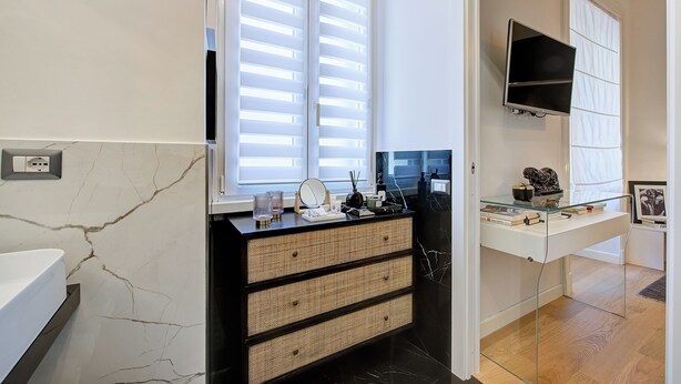 A modern bathroom with a white marble wall, a black vanity with a woven basket drawer, a glass shelf with decorative items, and a large mirror. - Prati Design Home (Roma)