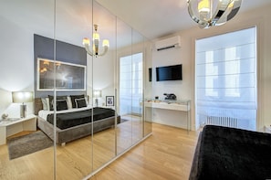 A modern bedroom with a bed, bedside tables, a desk, a TV, and a large mirror. - Prati Design Home (Roma)