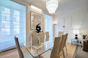 A modern dining area with a glass table and chairs, a chandelier, and a view through large windows. - Prati Design Home (Roma)