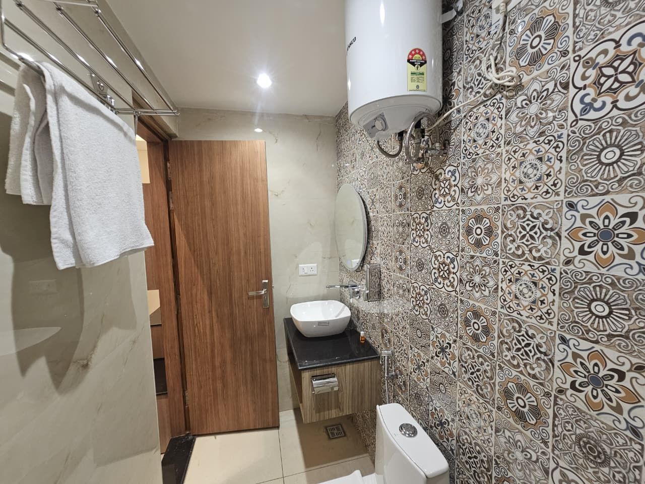 A bathroom with a wooden door, a white sink, a towel rack, and a wall with patterned tiles.