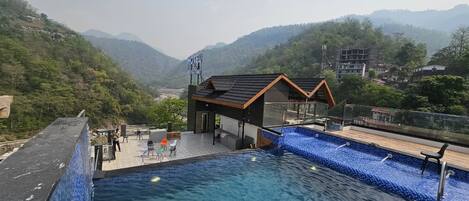 A hotel with a swimming pool, a covered area with seating, and a view of the surrounding hills.