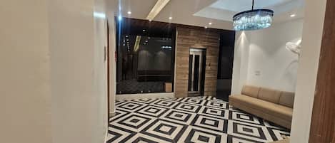 A hotel lobby with a geometric patterned floor, a reception desk, a sofa, and a chandelier.