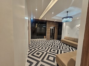 A hotel lobby with a geometric patterned floor, a reception desk, a sofa, and a chandelier.