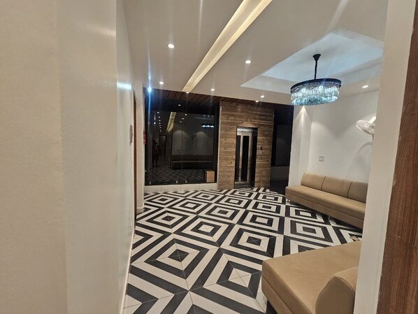 Un hall de hotel con piso de diseño geométrico, una recepción, un sofá y una araña.