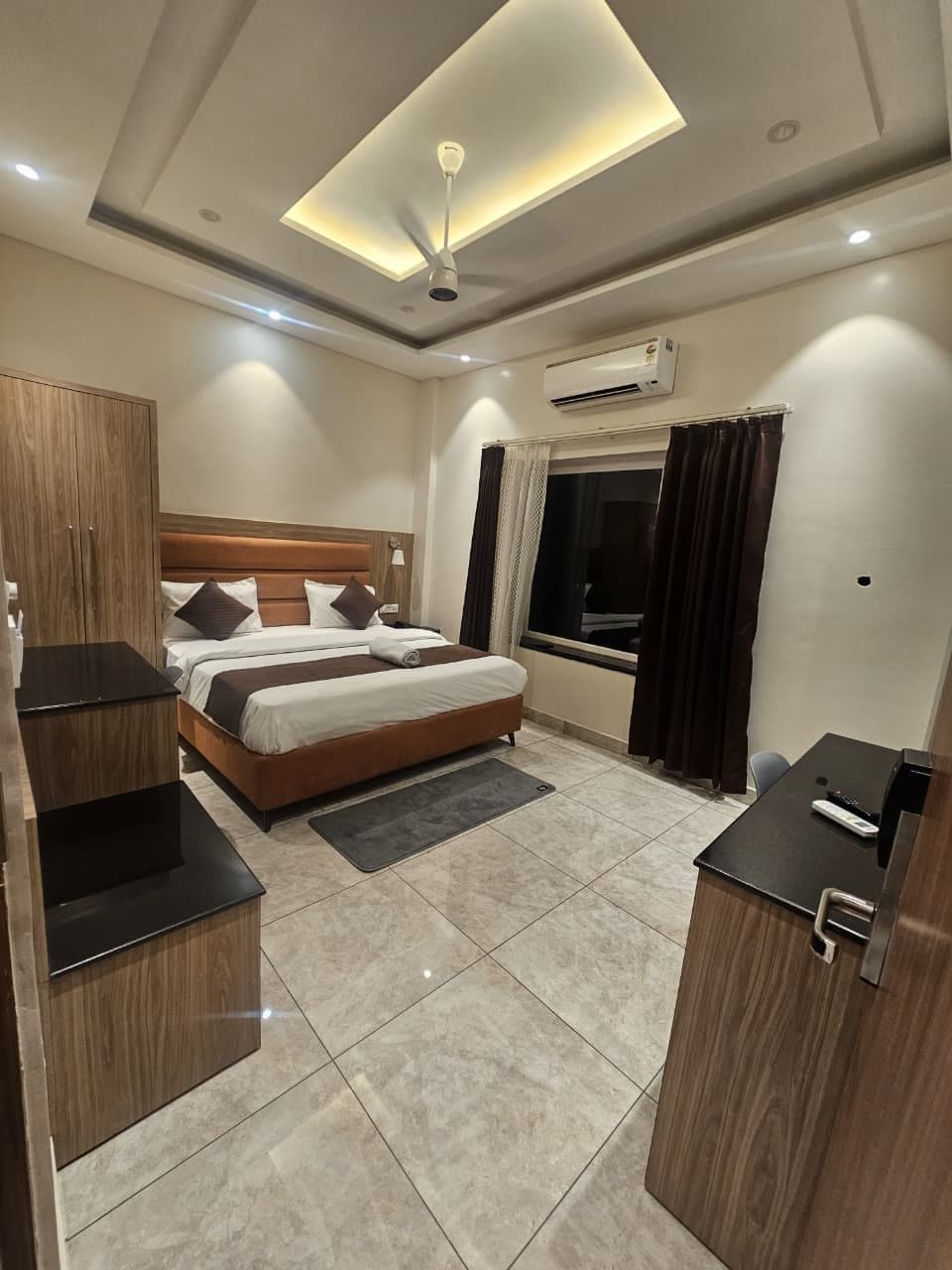 Ein Hotelzimmer mit Bett, Schreibtisch, Kleiderschrank, Klimaanlage und einem Vorhangfenster.