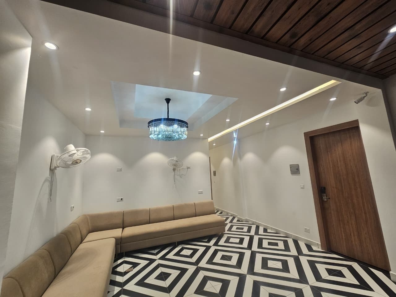 A modern interior with a geometric patterned floor, a beige sofa, a chandelier, and a wooden door.