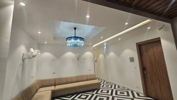 A modern interior with a geometric patterned floor, a beige sofa, a chandelier, and a wooden door.