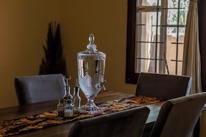 Un tavolo da pranzo con un contenitore di vetro decorativo, saliera e pepiera, e un sottopiatti colorato.