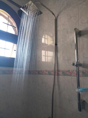 Una doccia dal design curvo, con un getto d'acqua visibile e una parete rivestita di piastrelle decorate con un motivo floreale.