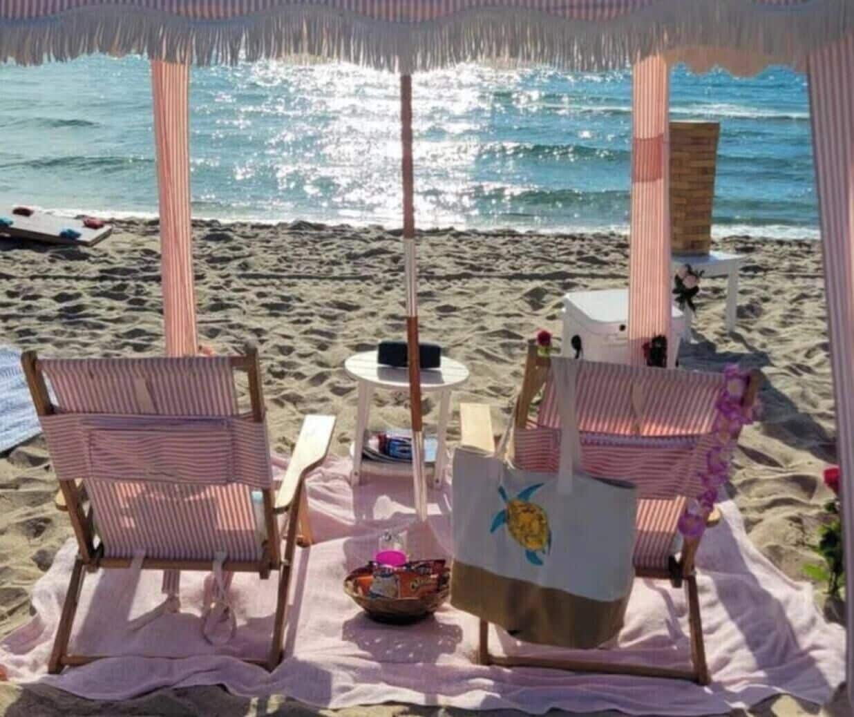 Un área de descanso en la playa con sillas a rayas, una mesa y una sombrilla.